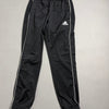 Pantaloni tuta sportivi adidas neri con profili bianchi distesi sul piano