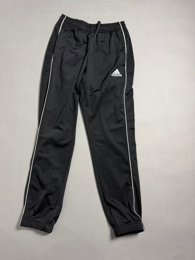 Pantaloni tuta sportivi adidas neri con profili bianchi distesi sul piano