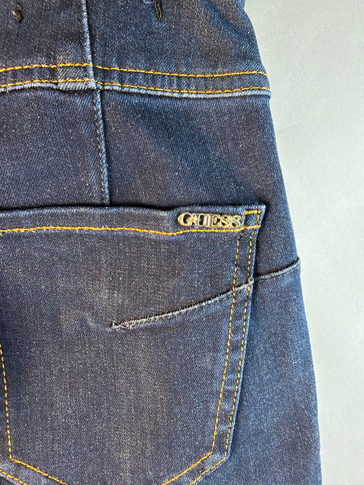 Dettaglio del logo metallico Guess sulla tasca posteriore dei jeans