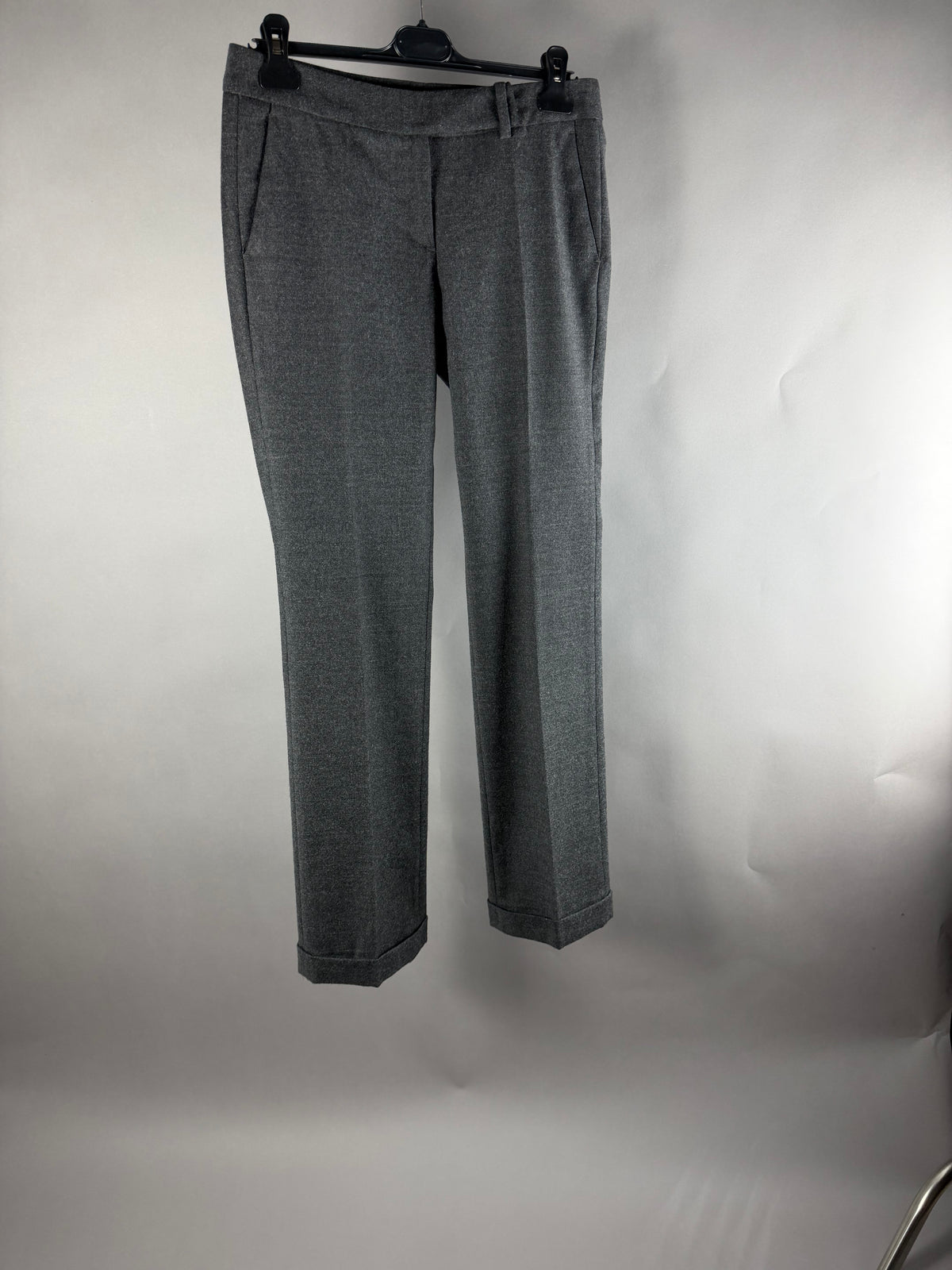 Pantaloni sartoriali da donna grigi con piega centrale e risvolto, vista frontale su gruccia