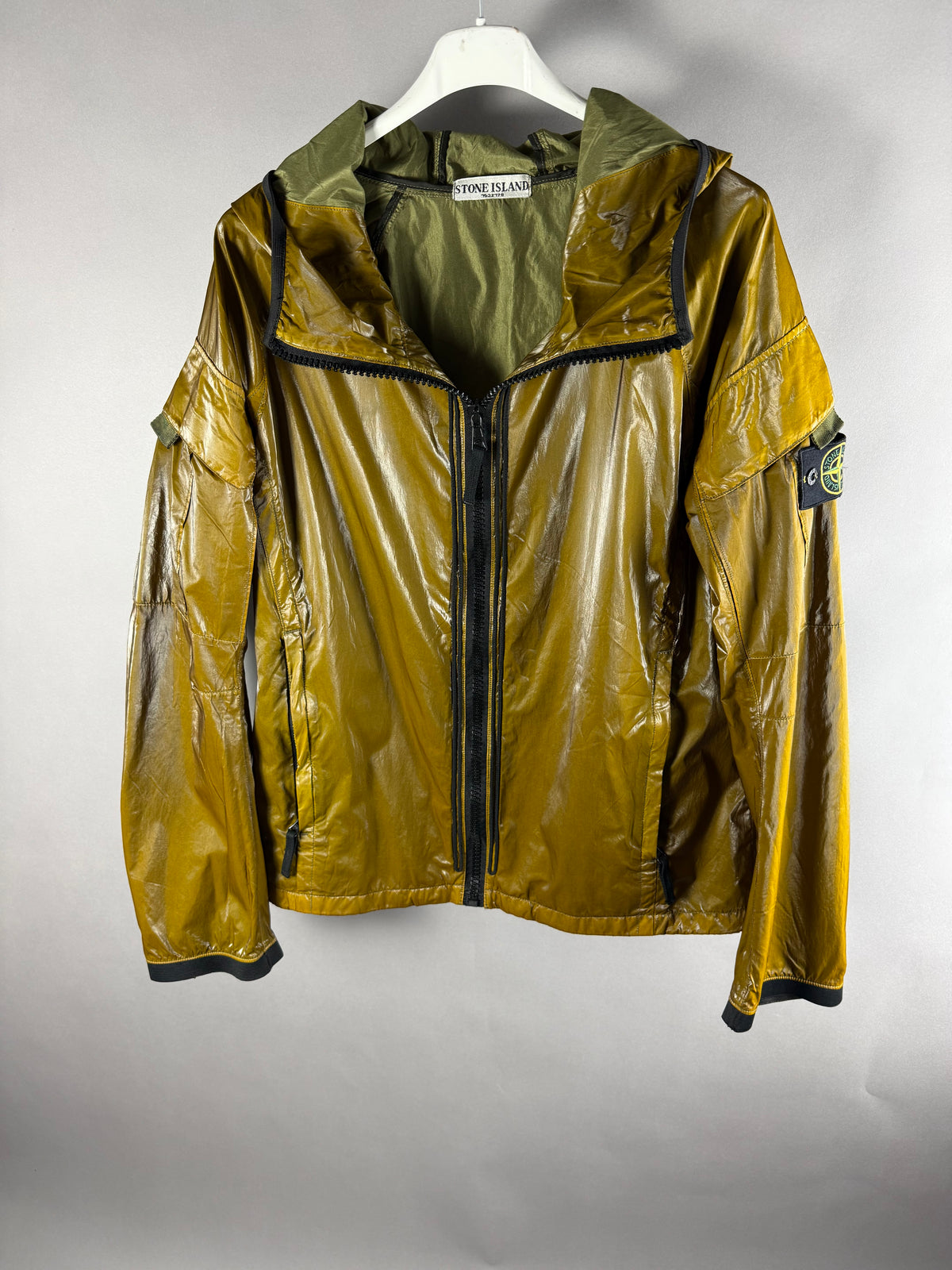 Vista frontale di giacca Stone Island verde oliva lucida con cappuccio e zip