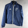 Vista frontale di giacca imbottita adidas blu con zip bianca e stemma JP
